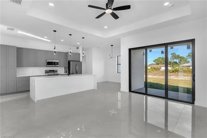 Kitchen featuring a center island with sink, gray cabinets, a raised ceiling, decorative light fixtures, and stainless steel appliances
