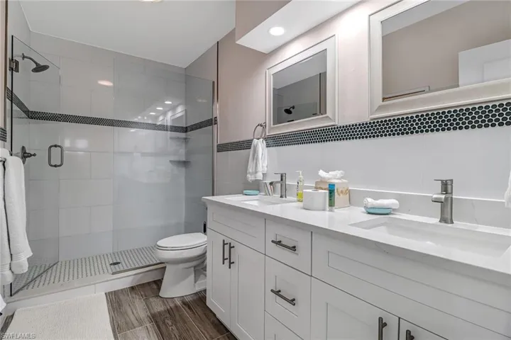 Full bath featuring double vanity, a stall shower, tile walls, and wood tiled floors