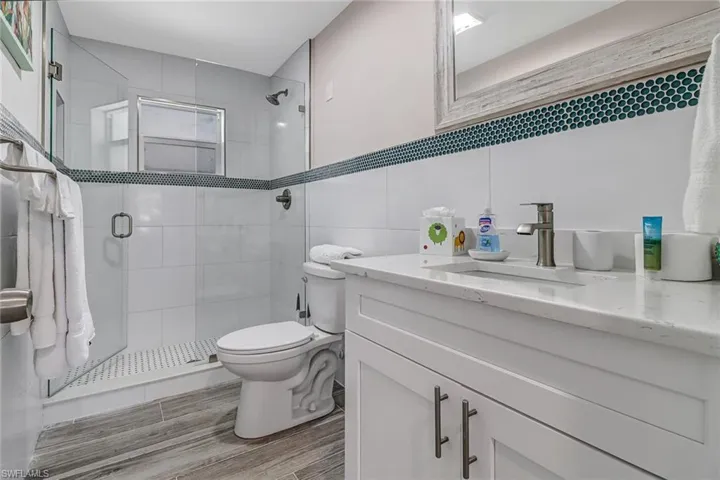 Full bath featuring vanity, a shower stall, tile walls, and wood finish floors