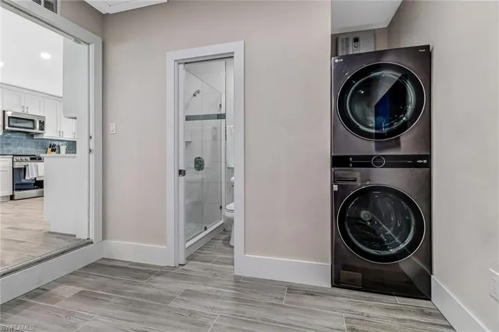 Laundry area with stacked washing machine and dryer, wood finish floors, and recessed lighting