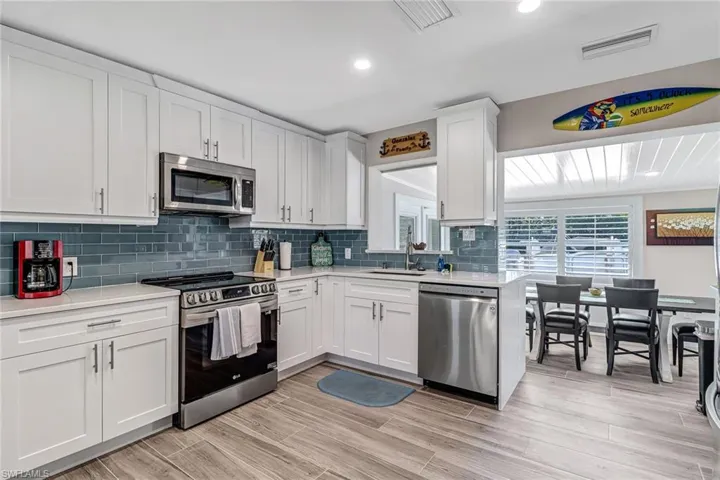 Kitchen featuring stainless steel appliances, white cabinets, light stone countertops, decorative backsplash, and wood finish floors