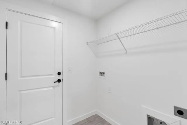 Utility room featuring a white panel door with black hardware, white wire shelving, and utility hookups