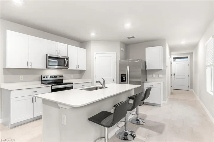 Kitchen featuring white cabinetry, sink, stainless steel appliances, a kitchen bar, and a center island with sink