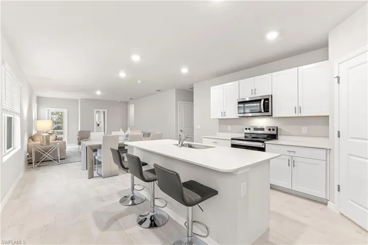 Kitchen featuring a center island with sink, white cabinetry, stainless steel appliances, and a breakfast bar area