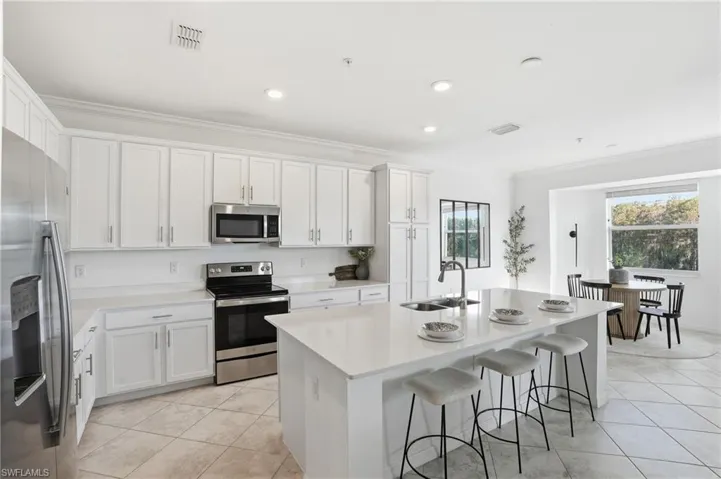 Kitchen featuring appliances with stainless steel finishes, ornamental molding, a center island with sink, a kitchen bar, and white cabinets
