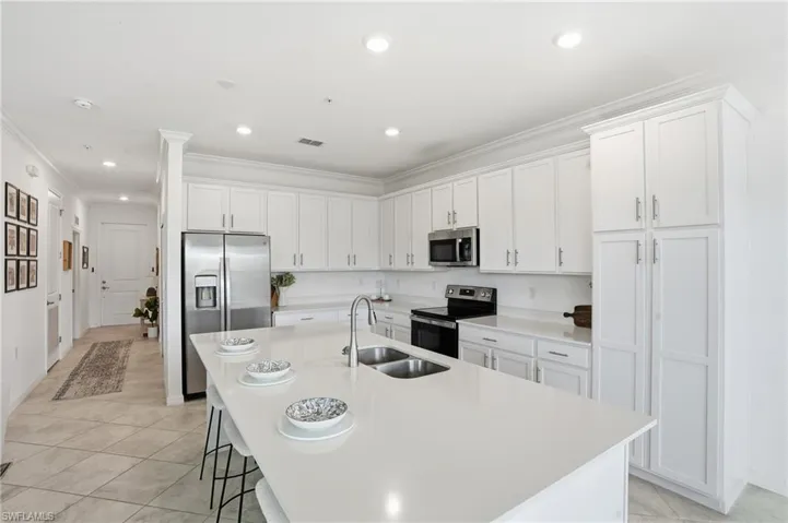 Kitchen with white cabinets, crown molding, a kitchen bar, stainless steel appliances, and light tile patterned floors