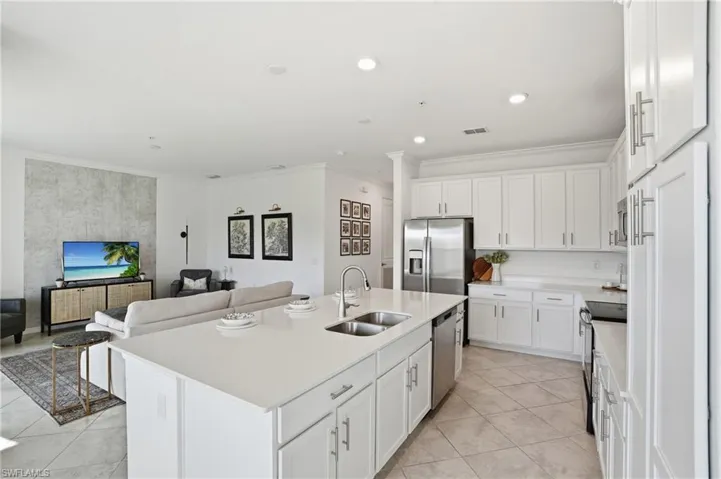 Kitchen featuring ornamental molding, open floor plan, white cabinets, appliances with stainless steel finishes, and a center island with sink