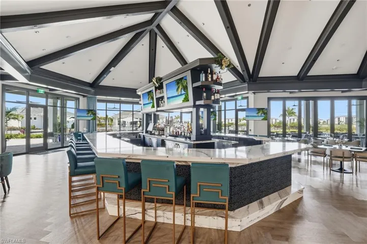 Bar area with beamed ceiling, high vaulted ceiling, healthy amount of natural light, light stone counters, and open floor plan