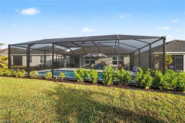 Rear view of property with a sunroom, a lawn, a lanai, and an outdoor pool