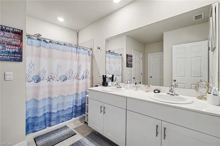 Bathroom with double vanity, curtained shower, and light tile patterned floors