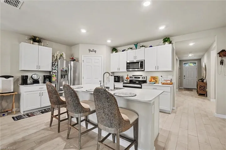 Kitchen featuring a breakfast bar area, white cabinets, light wood-style floors, stainless steel appliances, and recessed lighting