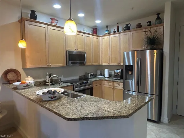Kitchen featuring a peninsula, granite countertop, stainless steel appliances, pendant lighting, and light wood finish cabinets