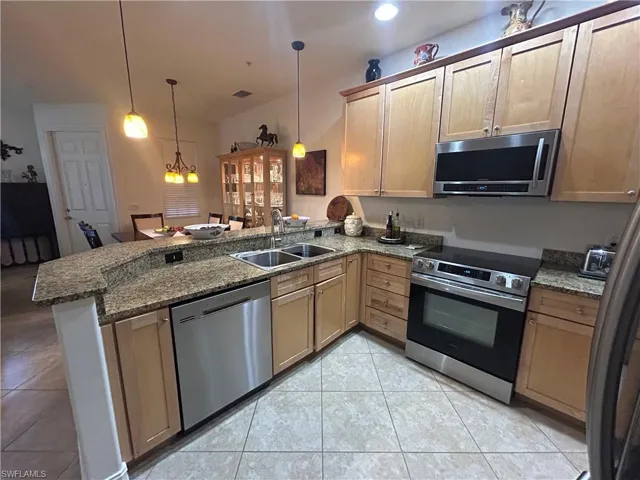 Kitchen featuring stainless steel appliances, light tile patterned floors, a peninsula, pendant lighting, and granite countwertop