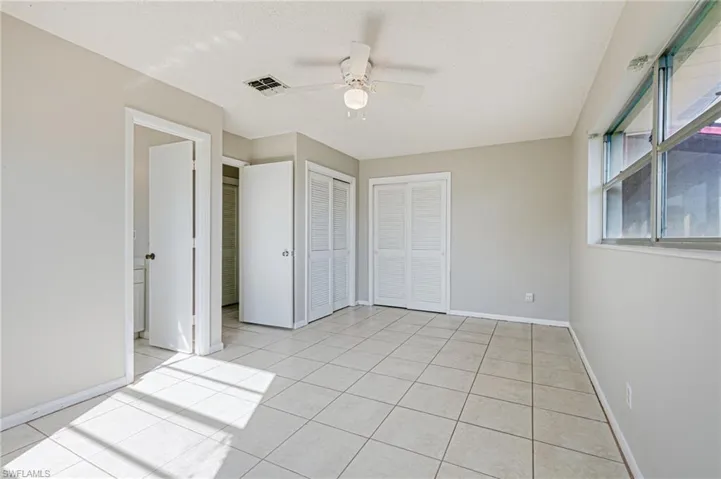 Unfurnished bedroom featuring ceiling fan, light tile patterned flooring, a textured ceiling, and two closets