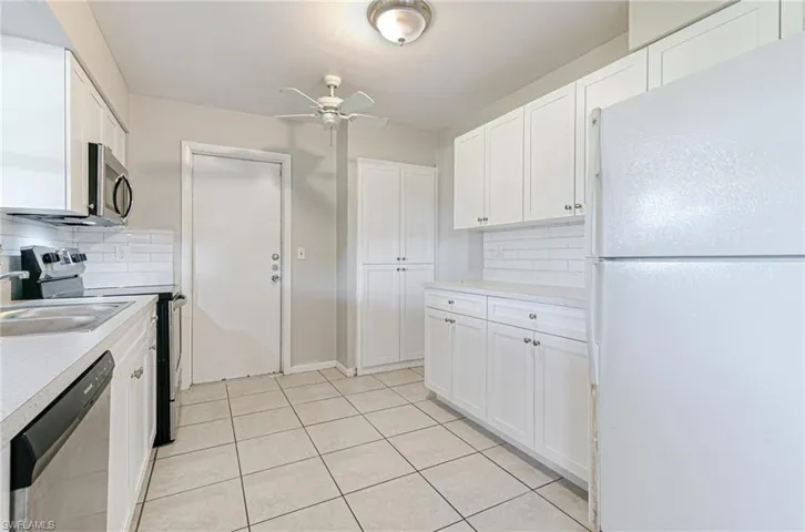 Kitchen with stainless steel appliances, light countertops, white cabinets, decorative backsplash, and a ceiling fan
