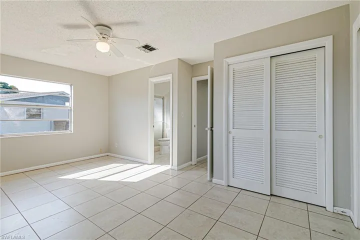 Unfurnished bedroom featuring a textured ceiling, a ceiling fan, a closet, ensuite bathroom, and light tile patterned floors