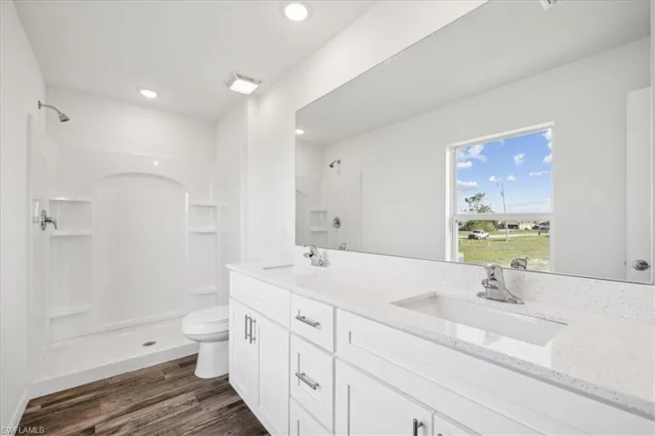 Bathroom featuring dual bowl vanity, walk in shower, hardwood / wood-style flooring, and toilet