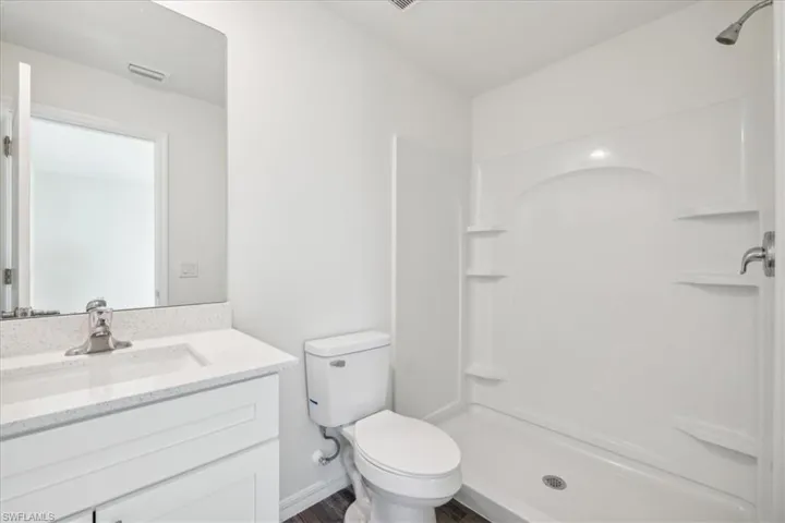 Bathroom with walk in shower, vanity with extensive cabinet space, hardwood / wood-style floors, and toilet