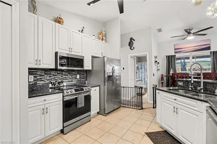 Kitchen with dark stone counters, white cabinetry, ceiling fan, appliances with stainless steel finishes, and lofted ceiling