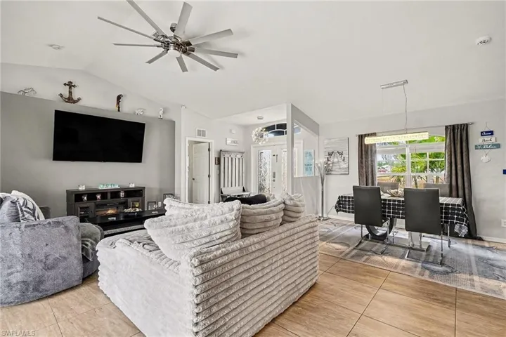 Living room with lofted ceiling, ceiling fan, light tile patterned flooring, and a chandelier