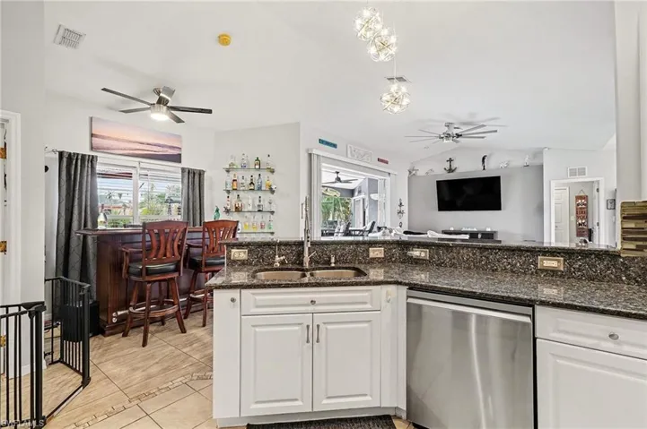 Kitchen with white cabinetry, dishwasher, dark stone counters, and lofted ceiling