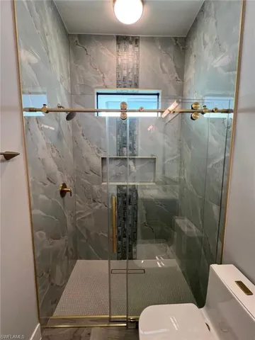 Full bathroom with toilet and a marble finish shower