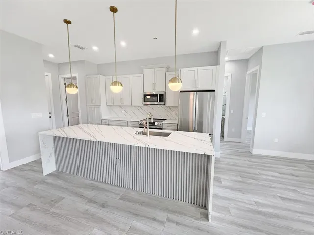 Kitchen featuring light stone counters, stainless steel appliances, a center island with sink, and decorative light fixtures