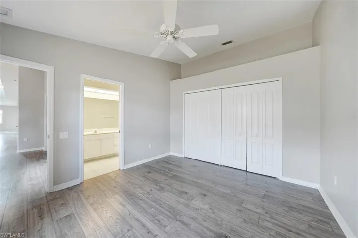 Unfurnished bedroom with ceiling fan, a closet, ensuite bath, and wood-type flooring