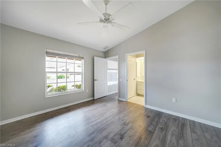 Unfurnished bedroom featuring hardwood / wood-style flooring, ensuite bathroom, ceiling fan, and vaulted ceiling