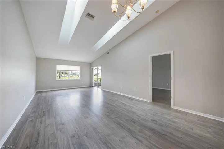 Spare room featuring high vaulted ceiling, wood-type flooring, an inviting chandelier, and a skylight