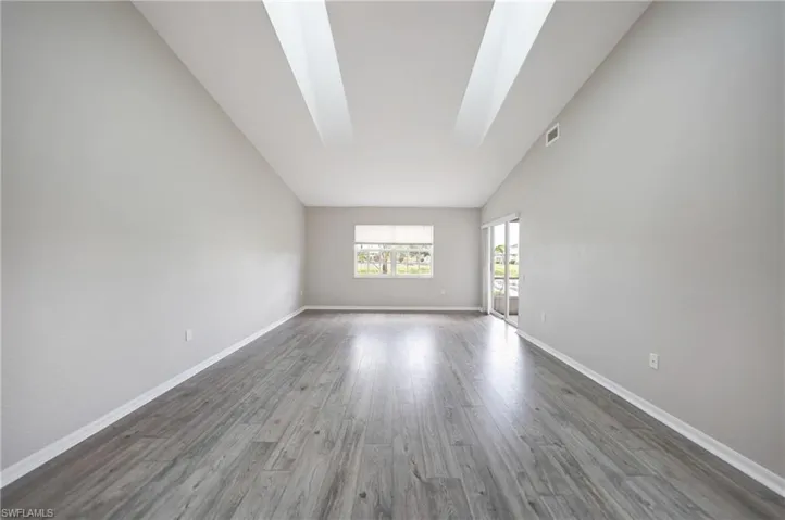 Unfurnished room featuring hardwood / wood-style floors and vaulted ceiling with skylight