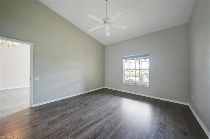 Spare room with high vaulted ceiling, ceiling fan with notable chandelier, and dark hardwood / wood-style flooring