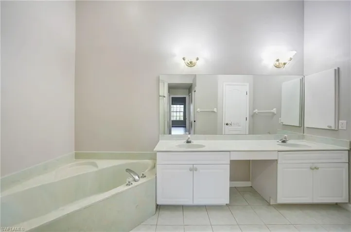 Bathroom with dual bowl vanity, tile floors, and a bathing tub