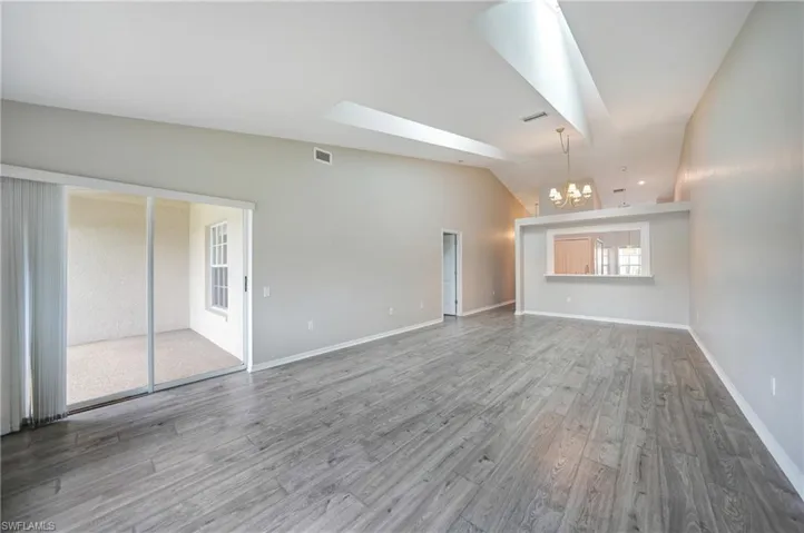 Empty room featuring vaulted ceiling, hardwood / wood-style floors, and a chandelier