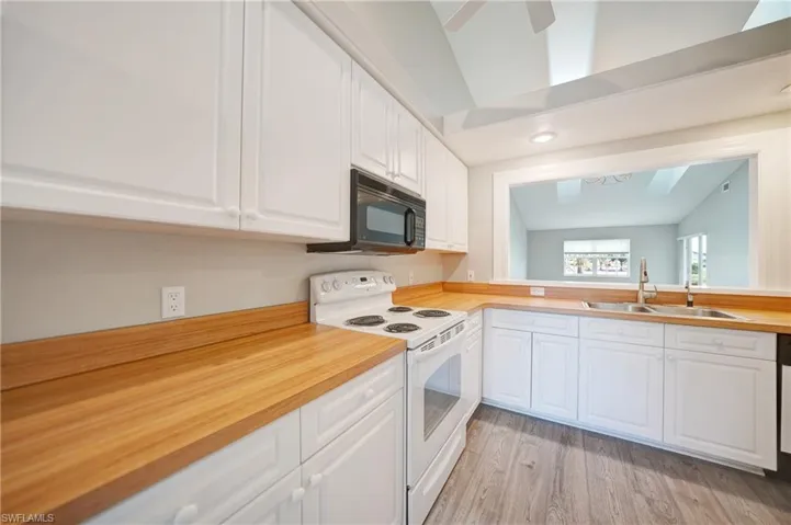 Kitchen featuring vaulted ceiling, light wood-type flooring, white electric range oven, white cabinets, and sink