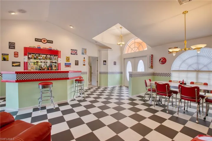 Dining room with dark floors, a dry bar, a chandelier, high vaulted ceiling, and french doors