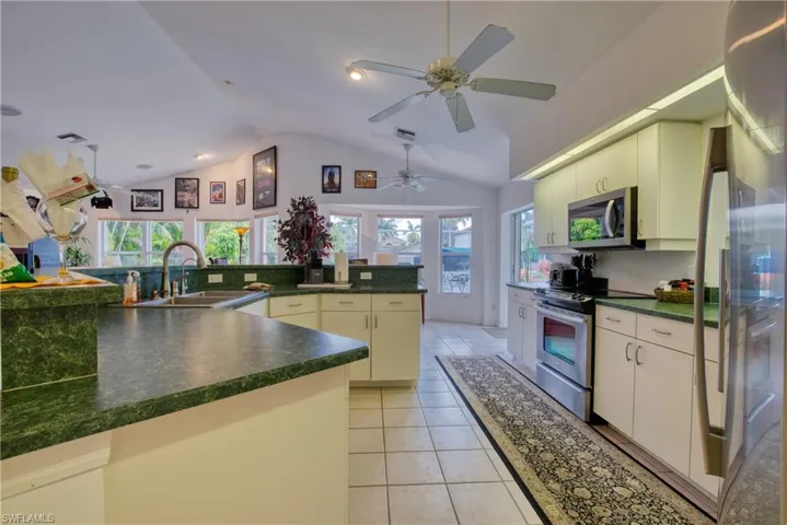 Kitchen with stainless steel appliances, dark countertops, lofted ceiling, plenty of natural light, and light tile patterned floors