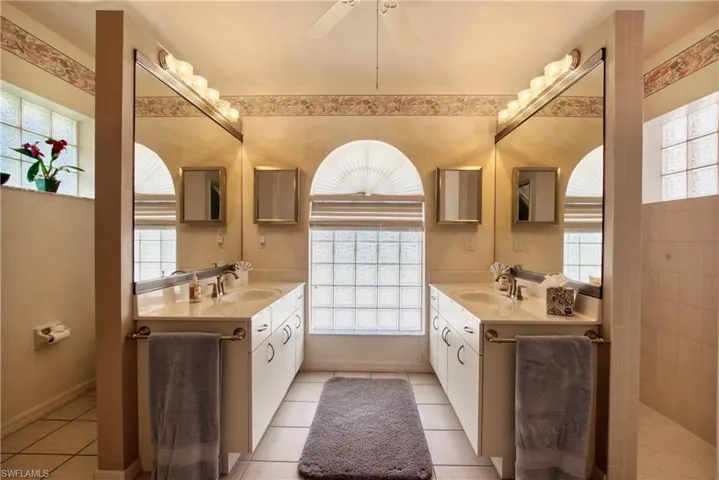 Bathroom featuring plenty of natural light, light tile patterned floors, and two vanities