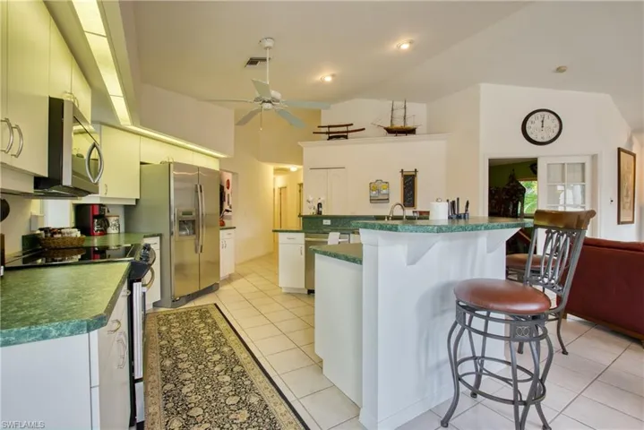 Kitchen featuring stainless steel appliances, a breakfast bar area, light tile patterned floors, a center island with sink, and vaulted ceiling