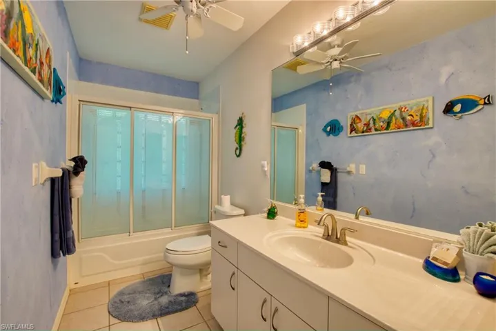 Full bathroom featuring vanity, enclosed tub / shower combo, light tile patterned flooring, and a ceiling fan