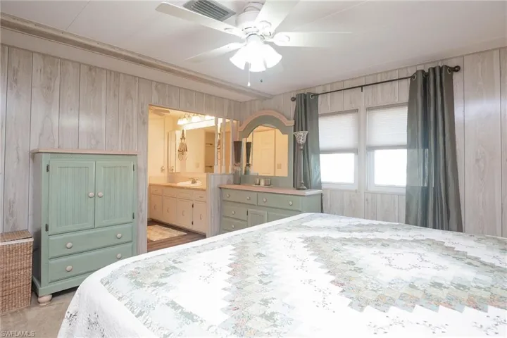 Bedroom featuring wood walls, ensuite bathroom, sink, ceiling fan, and light colored carpet