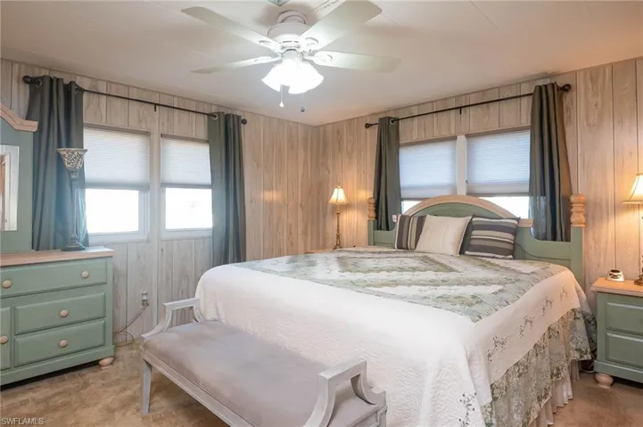 Bedroom with ceiling fan, wooden walls, and light carpet