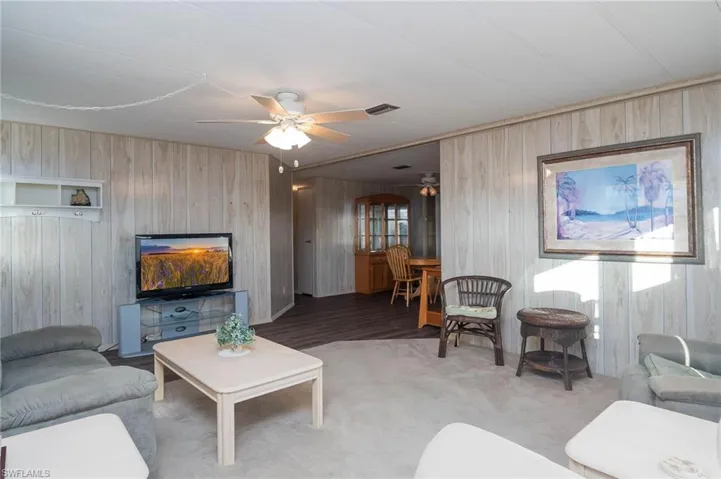 Living room with carpet floors, ceiling fan, and wooden walls