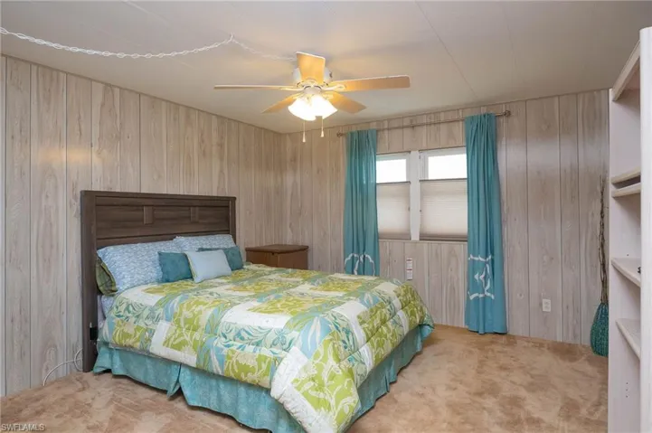 Carpeted bedroom featuring ceiling fan and wood walls