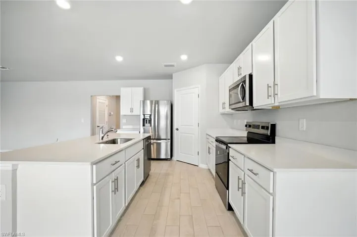 Modern kitchen featuring white cabinetry, light-toned countertops, stainless steel appliances, and wood-finish flooring