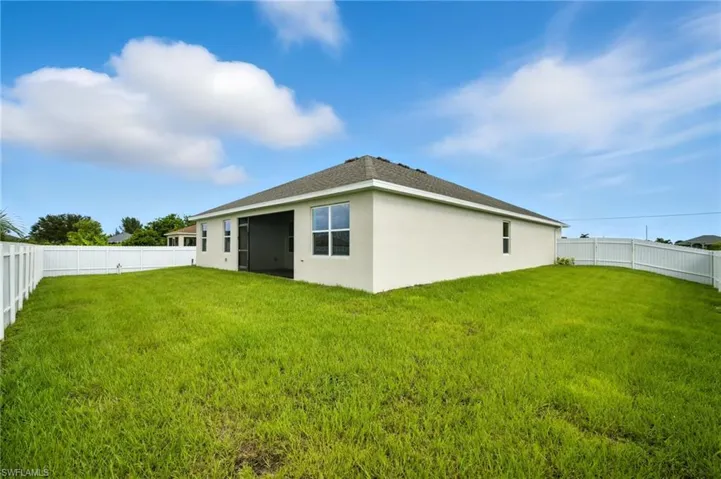 Expansive grassy backyard featuring a full white privacy fence