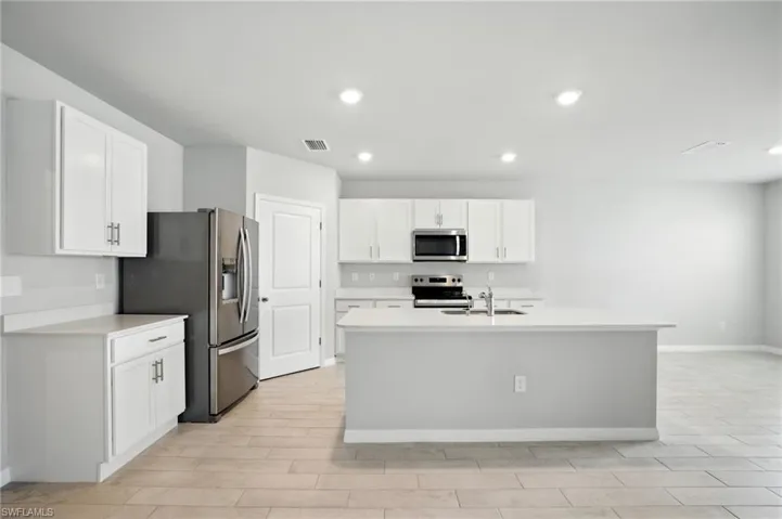 Modern kitchen featuring white cabinetry, stainless steel appliances, a center island with sink, ample counter space, and wood-finish flooring