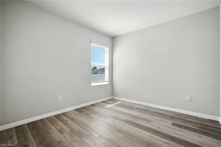 Room featuring wood-finish flooring, light gray walls, white baseboards, and a window with horizontal blinds