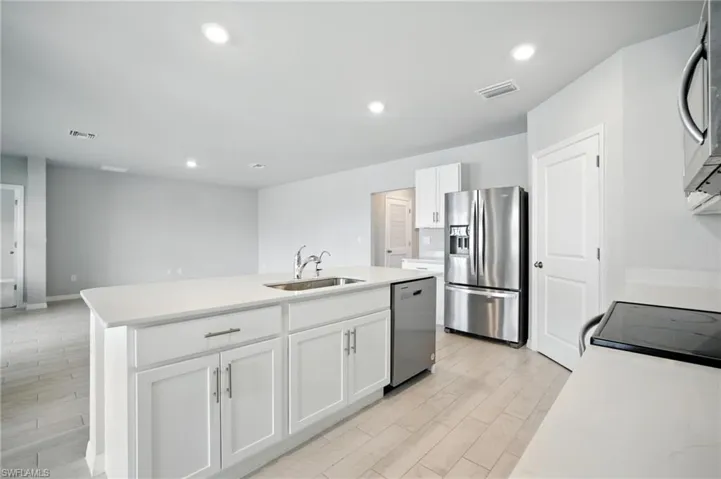 Kitchen island featuring a stainless steel sink with a high-arc faucet, white shaker cabinetry, and a light-toned countertop