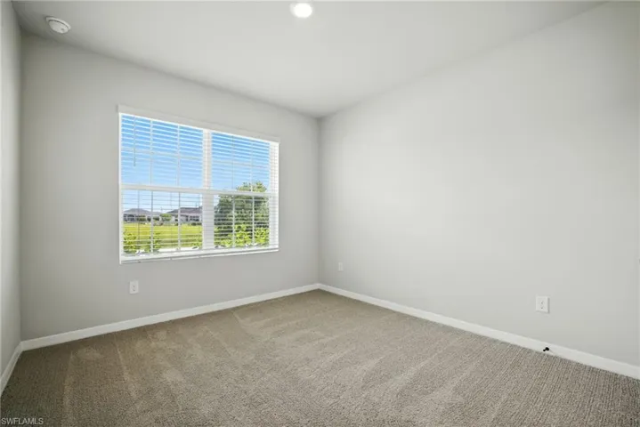 Light-filled interior space with neutral-toned walls, plush carpet flooring, and a large window featuring horizontal blinds